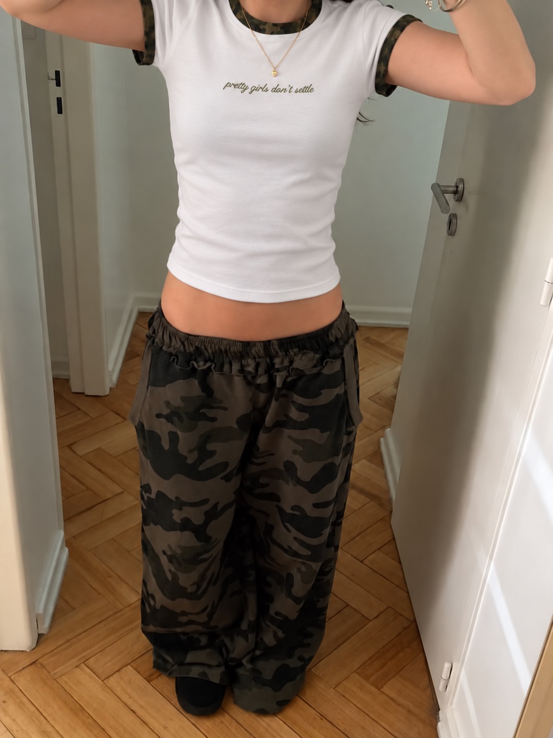 Pretty Girls Don't Settle white and camo baby tee worn in a doorway with camo pants