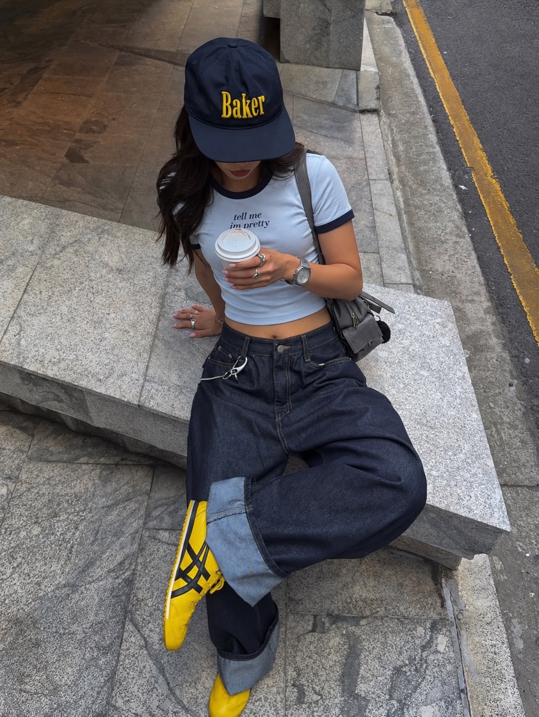 Tell Me I'm Pretty blue and navy baby tee worn seated on a street ledge with wide-leg jeans